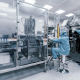 Индустриальная фотосъёмка линии по разливу медицинских препаратов с двумя лаборантами, контролирующими производственный процесс