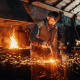 Фотография кузнеца за работой в кузнечном цеху возле наковальни с разлетающимися огненными искрами во время ковки металлической детали