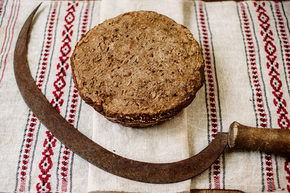 Буханка домашнего пшеничного хлеба на льняном полотенце с серпом.