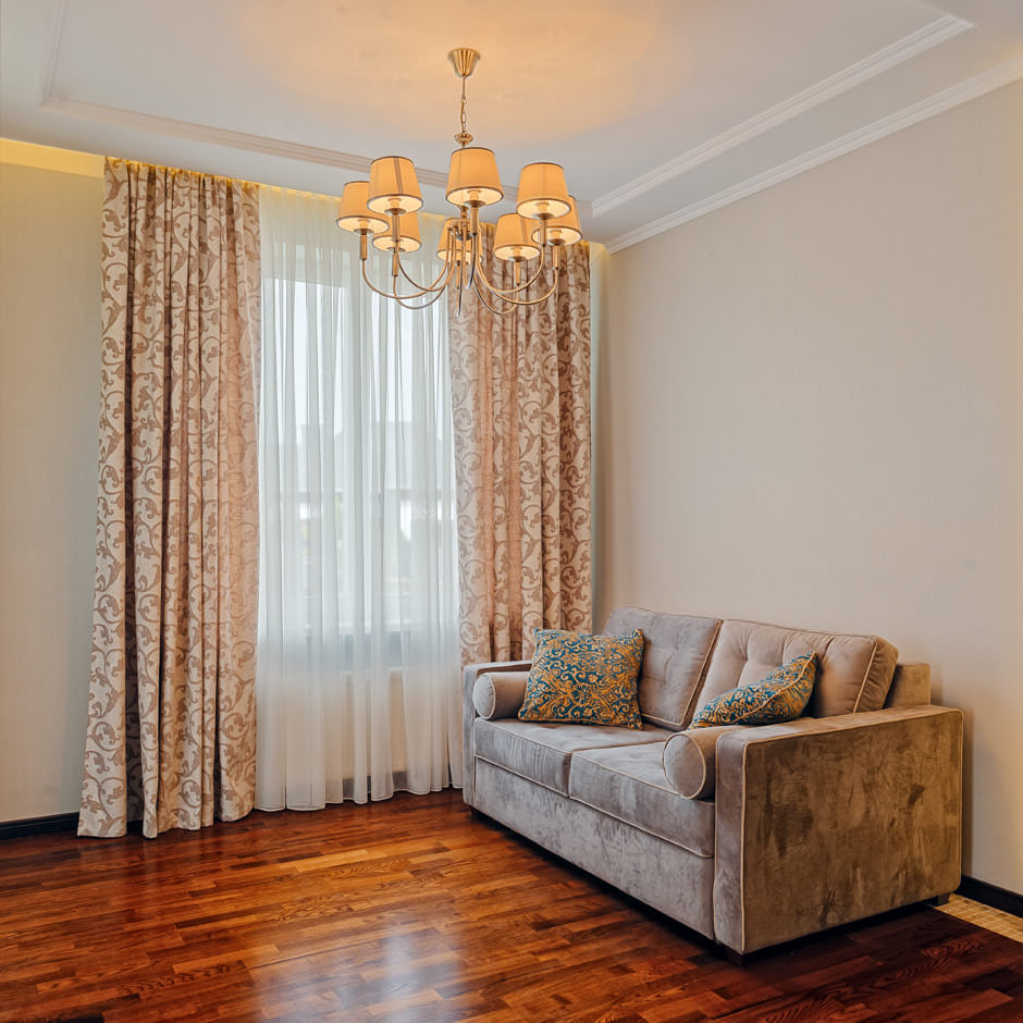 Фото интерьера зала в классическом стиле, вид на диван с подушками и большое окно со шторами