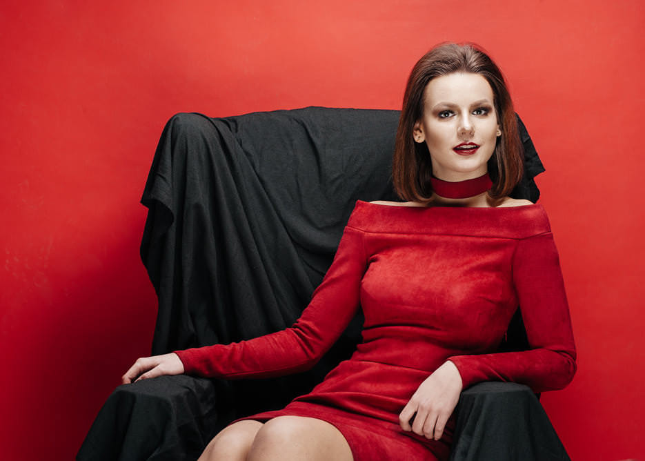Студийный портрет девушки с макияжем в красном платье в черном кресле, результат творческого процесса организации и проведения фотосессии