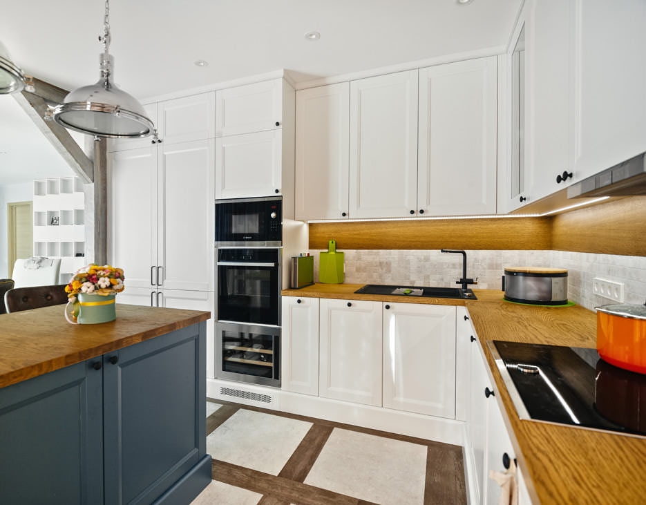 Фотография кухонной мебели белого цвета с островом, столешницей, шкафами и встроенной бытовой техникой