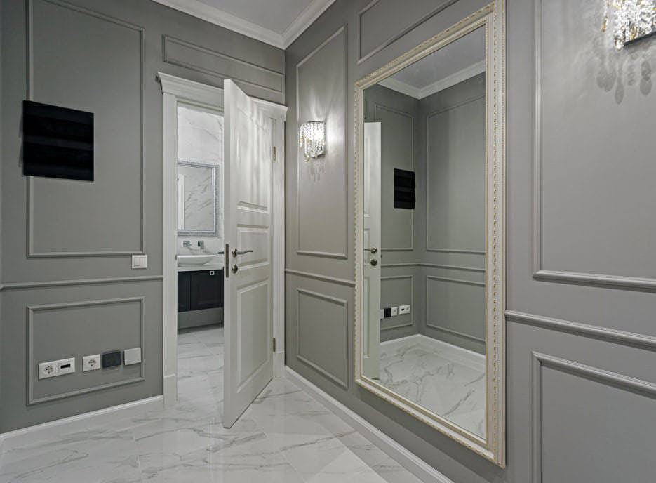 Серый коридор квартиры с большим зеркалом в раме и светильником на стене с видом на ванную комнату через дверь