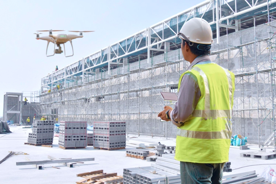 Беспилотная аэрофотосъёмка строительного объекта, пилот управляет летательным аппаратом на фоне возводимой бетонной конструкции
