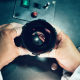 Промышленная фотография производственного предприятия Zeiss-БелОМО, руки работника отдела технического контроля качества держат фото-объектив