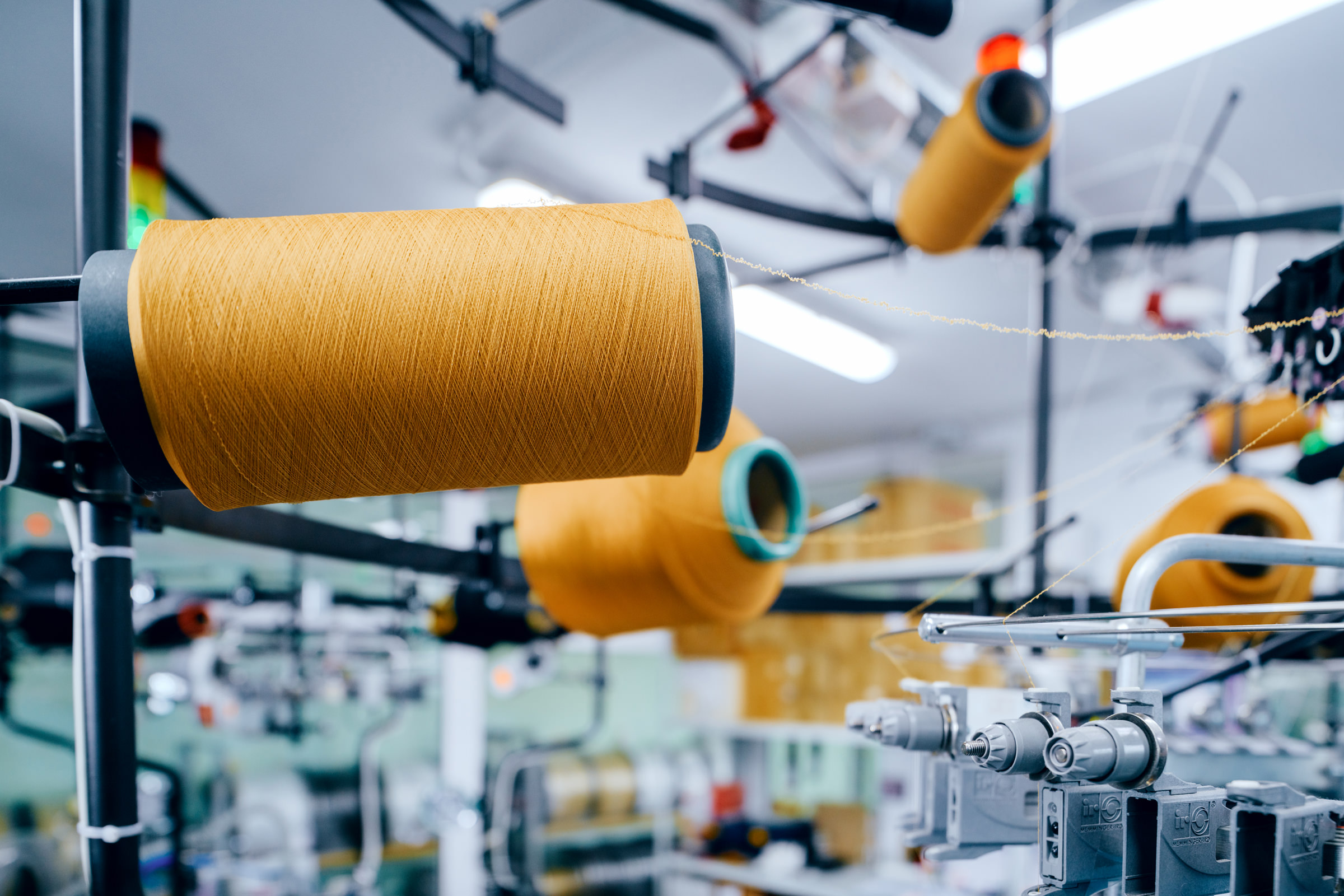 Фотография катушек с оранжевыми нитками на ткацком станке на фабрике по производству медицинских бинтов и бандажей в городе Молодечно, Беларусь